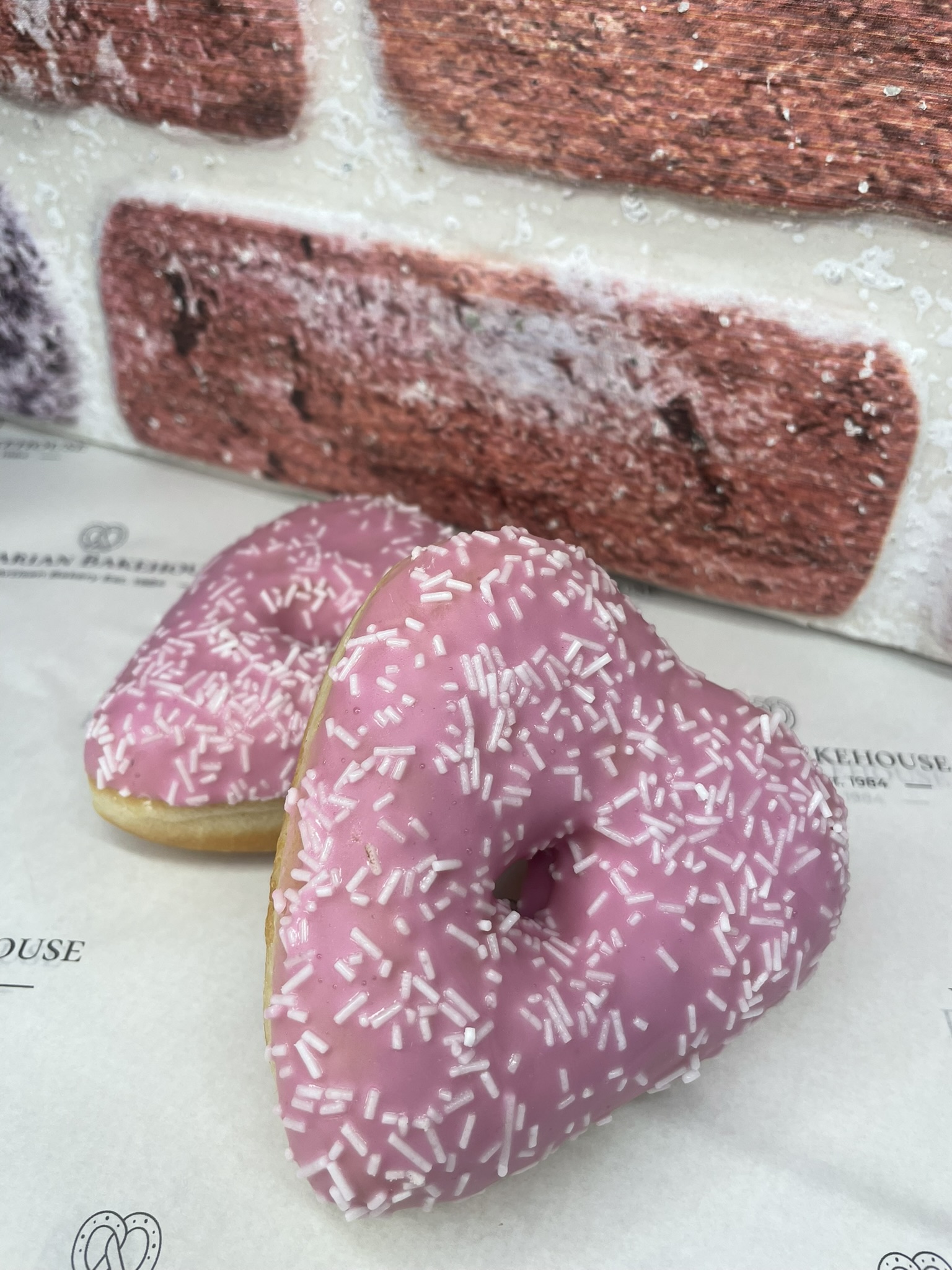 soft heart shaped doughnut topped with pink frosting and white sprinkles.