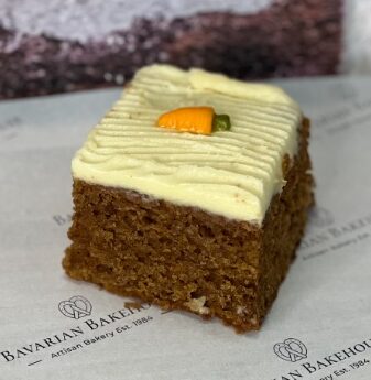 Rich, spiced carrot cake sponge square, topped with a tangy but sweet cream cheese frosting and a small carrot sweet melt shape.