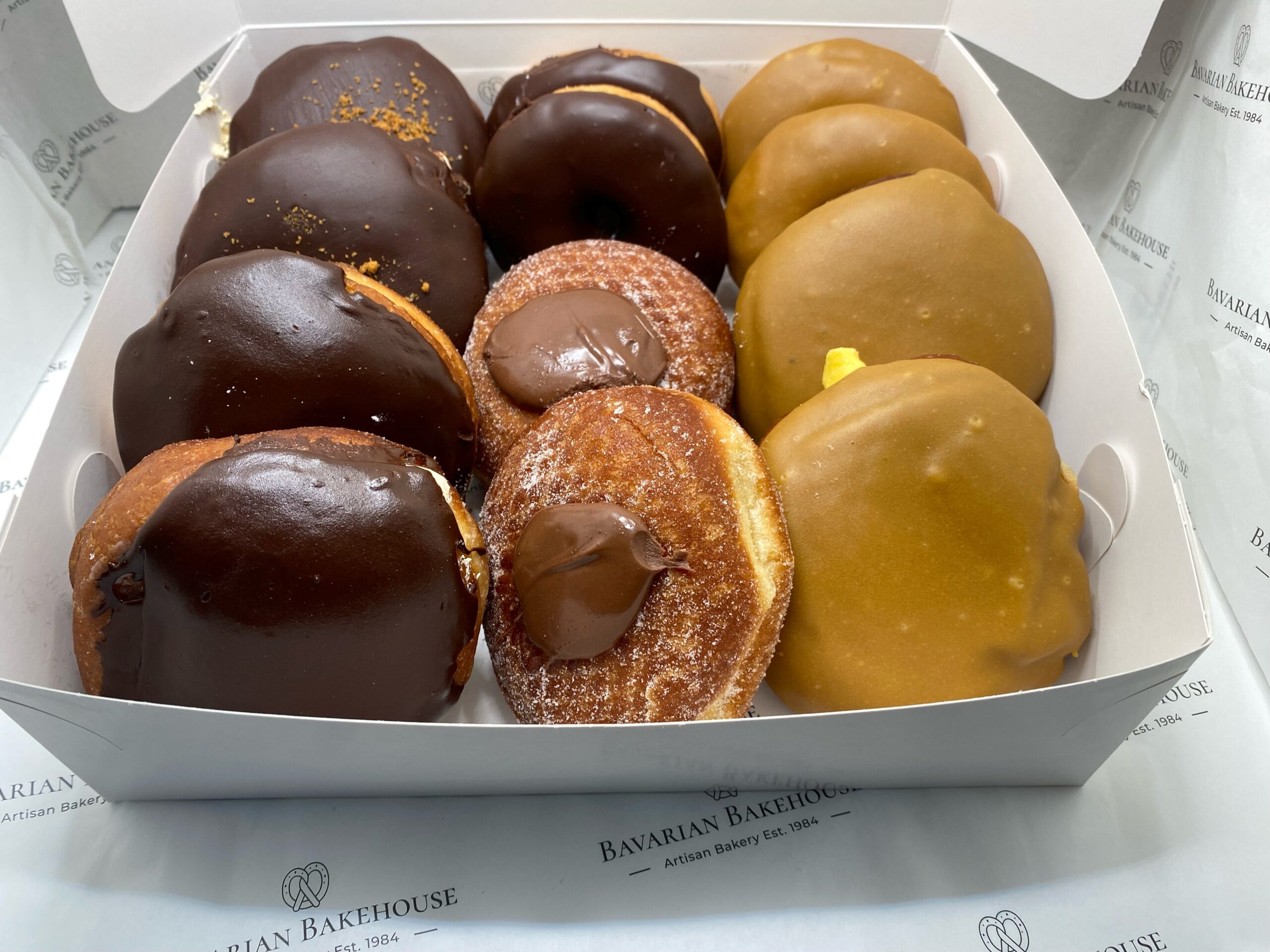 12 soft doughnuts: 2 chocolate ring, 2 fudge ring, 2 sugared filled with Nutella, 2 Caramel Creme filled and topped with Chocolate fudge frosting and Biscoff crumble, 2 custard cream filled with thick fudge icing and 2 custard cream filled with chocolate topping.