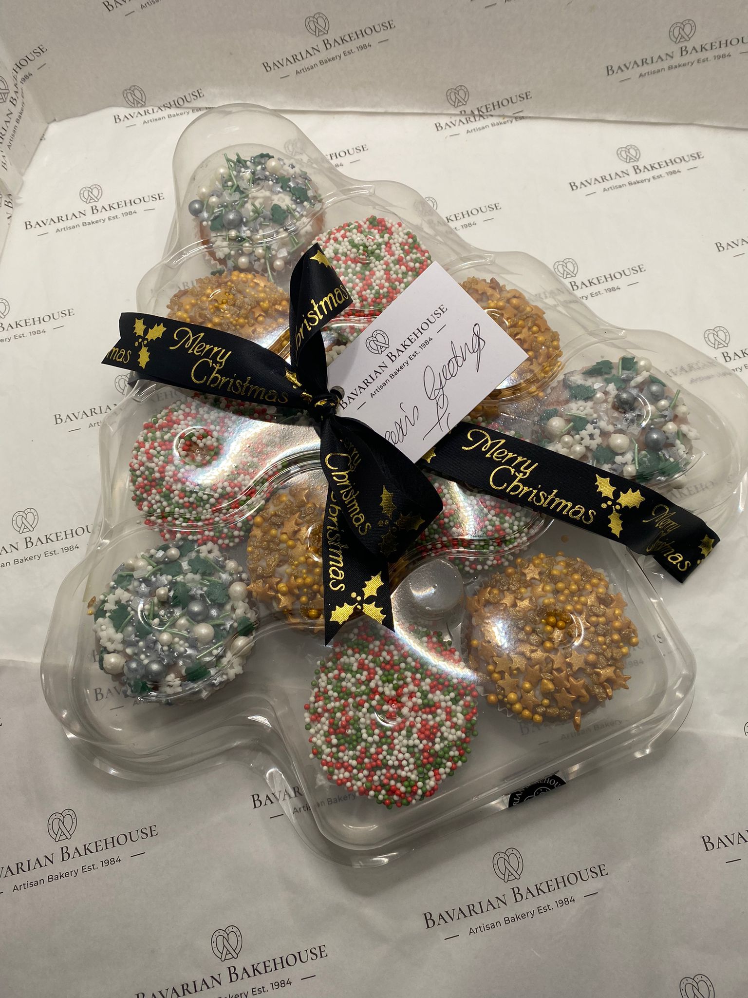 12 vanilla sponge cakes topped with fondant and sprinkles in a plastic xmas tree box with ribbon and a card