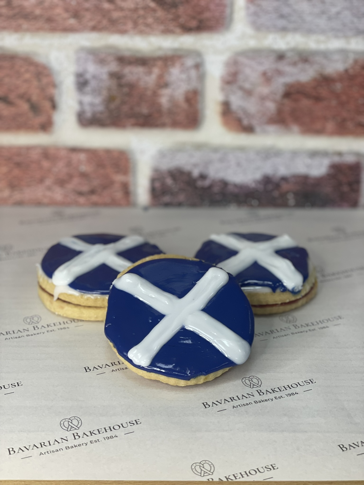 2 soft buttery shortbread biscuits, a jam filling topped with blue icing and a white cross
