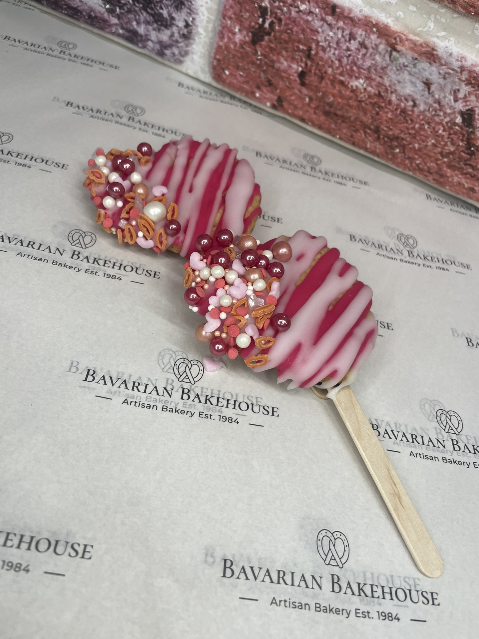 crumbly biscuit heart, secured to a lolly pop stick by chocolate, covered in pink frosting, white drizzle and themed sprinkles. 2 in a box.