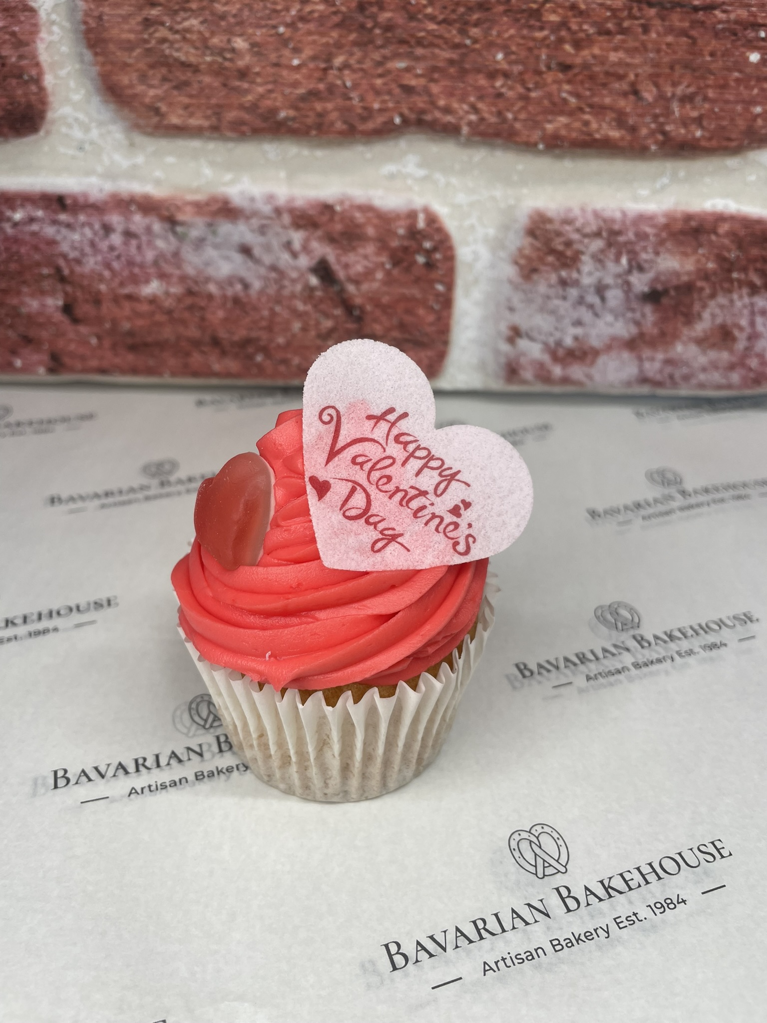 Vanilla cupcake with red vanilla frosting topped with jelly heart sweet and an edible heart topper saying happy valentines. Gift box of 6.