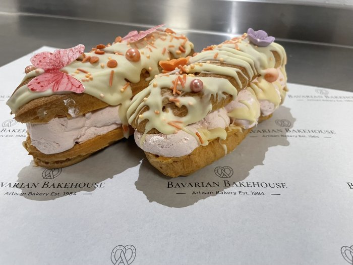 half sized choux pastry eclair wfilled with strawberry crea, decorated with a white choc drizzle, sprinkles, fondant flowers and rice paper butterflies
