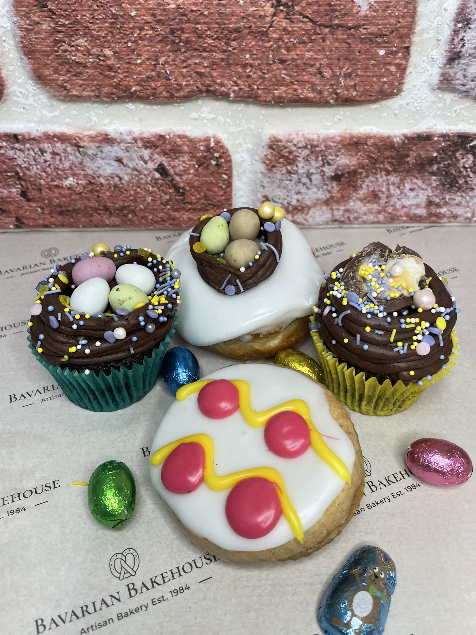 Easer lemon curd filled empire, decorated to look like an easter egg. 2 chocolate cupcakes, topped with choc frosting in shape of a nest with mini eggs or half a creme egg decoration and sprinkles, a doughnut filled with Nutella cream, topped with white fondant, sprinkles, and a choc frosting nest with mini eggs.