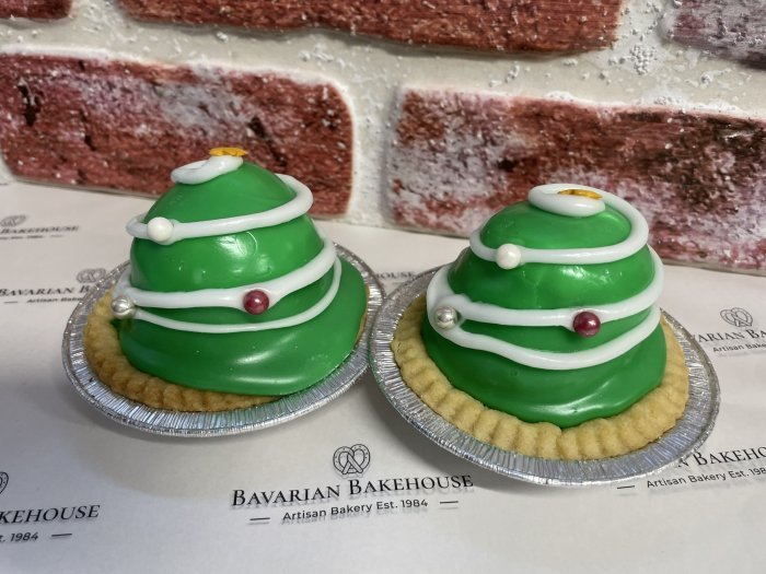 vegan pastry tart base, filled with a mound of vegan cream, lime jam, covered in green fondant, a white fondant swirl, large round edible coloured pearls for baubles and a gold star sprinkle on top