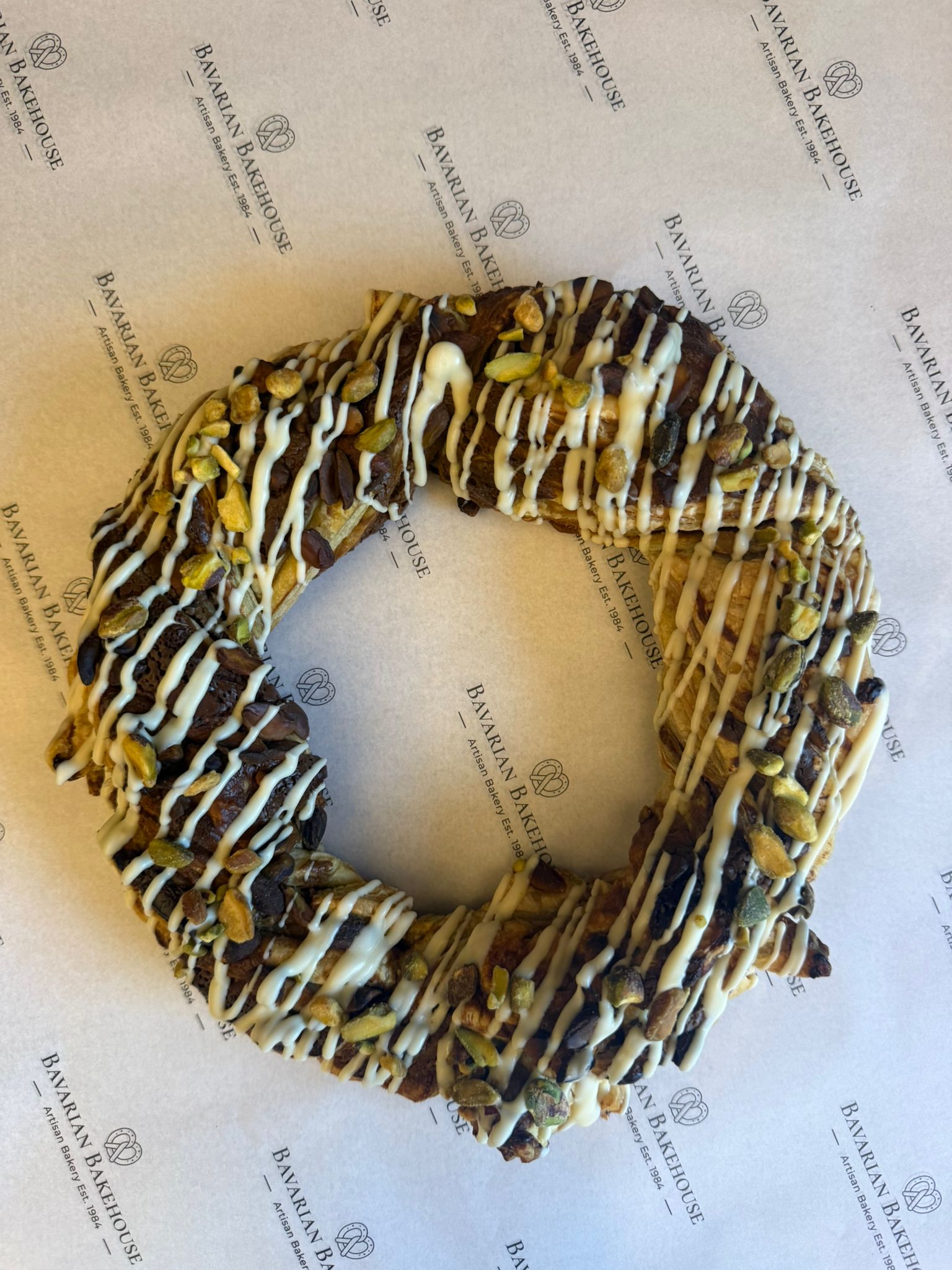 flaky puff pastry, pleated into a wreath, filled with pistachio paste, topped with white chocolate drizzle and chopped pistachio nuts
