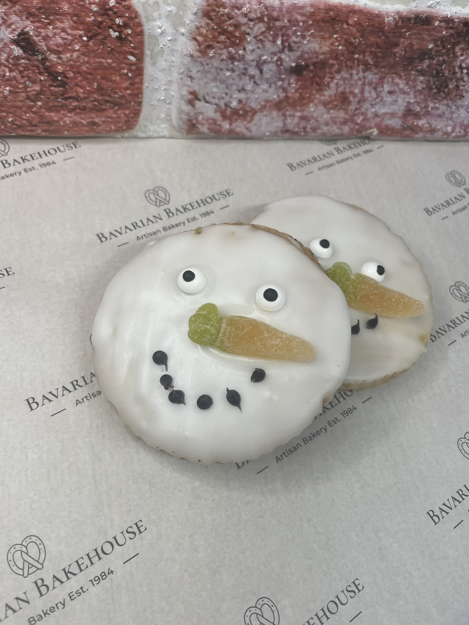 Vegan empire biscuit with jam in between, white fondant on top, with a vegan jelly carrot sweet as a nose, fondant eyes and black fondant coal dots for a mouth