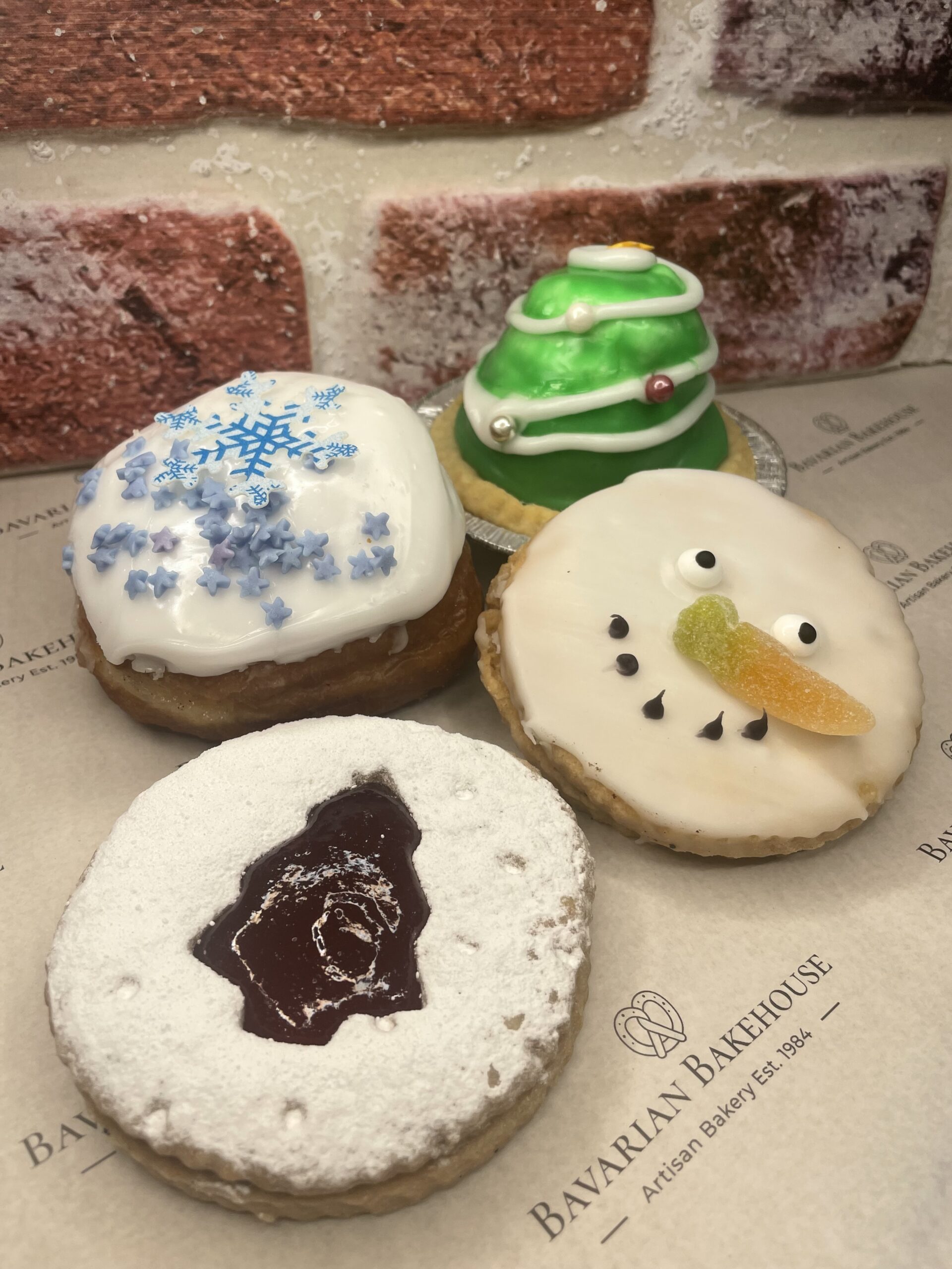 snowman face empire, a Linzer biscuit with tree cut out, a white findant snowflake topper doughnut and a green vegan tart decorated to look like a Christmas tree. Please refer to gallery images for more detailed information.