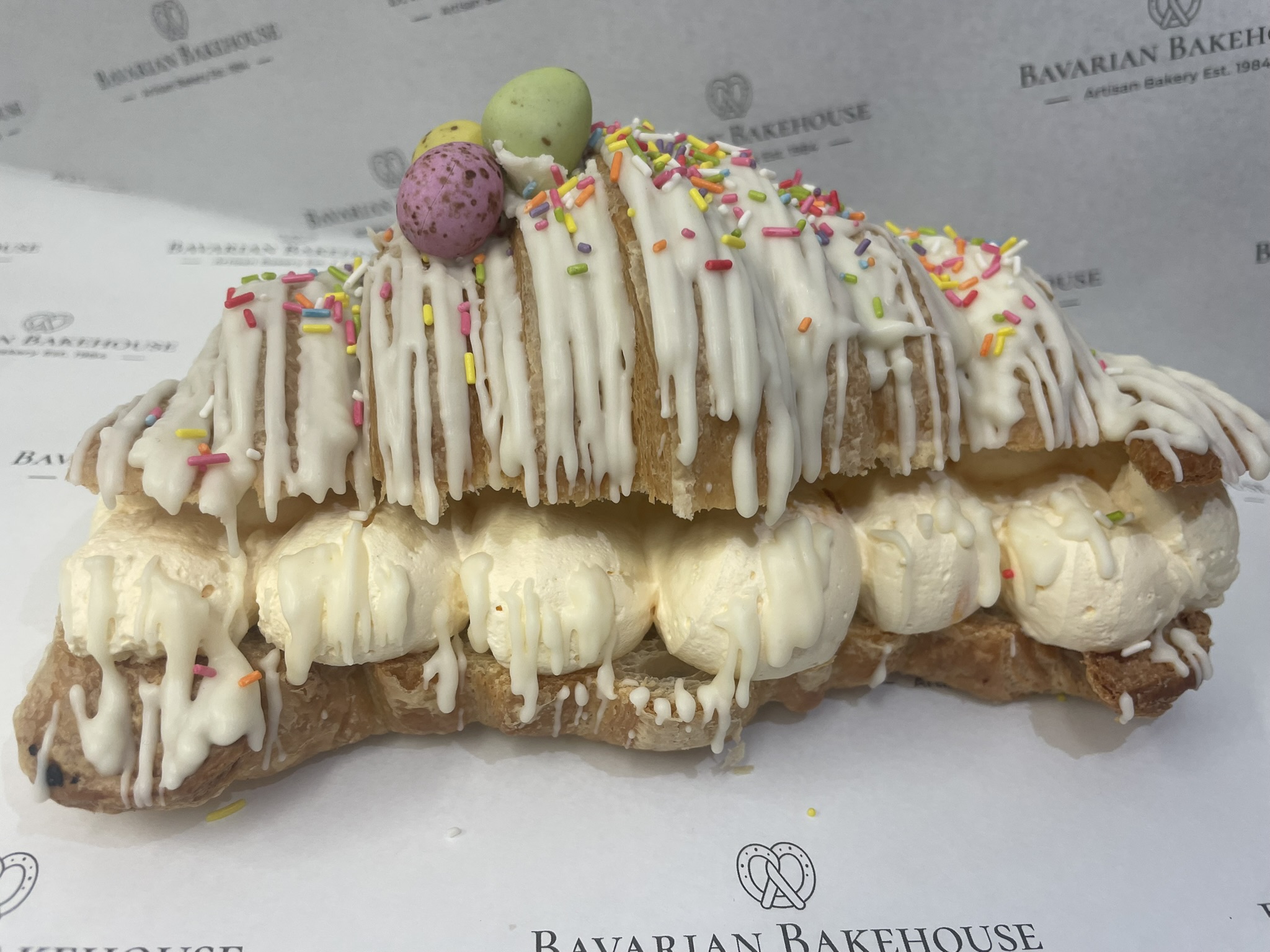 large flaky croissant cut open and filled with orange flavoured cream. Topped with a white choc drizzle and easter sprinkles, mini eggs of an edible topper. Please note toppings may vary.